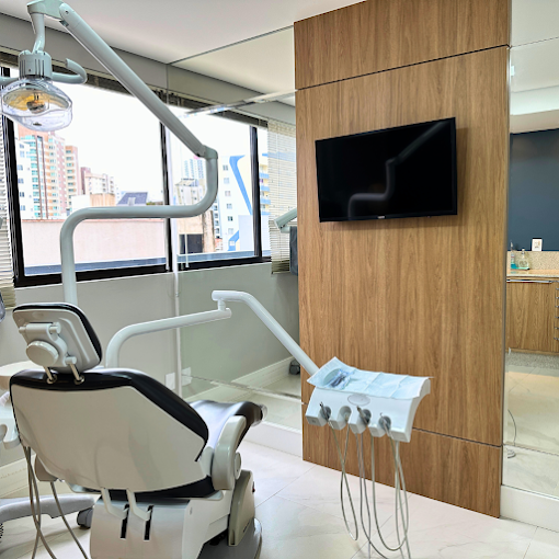 Consultório odontológico com cadeira e equipamentos, iluminado por janela ampla