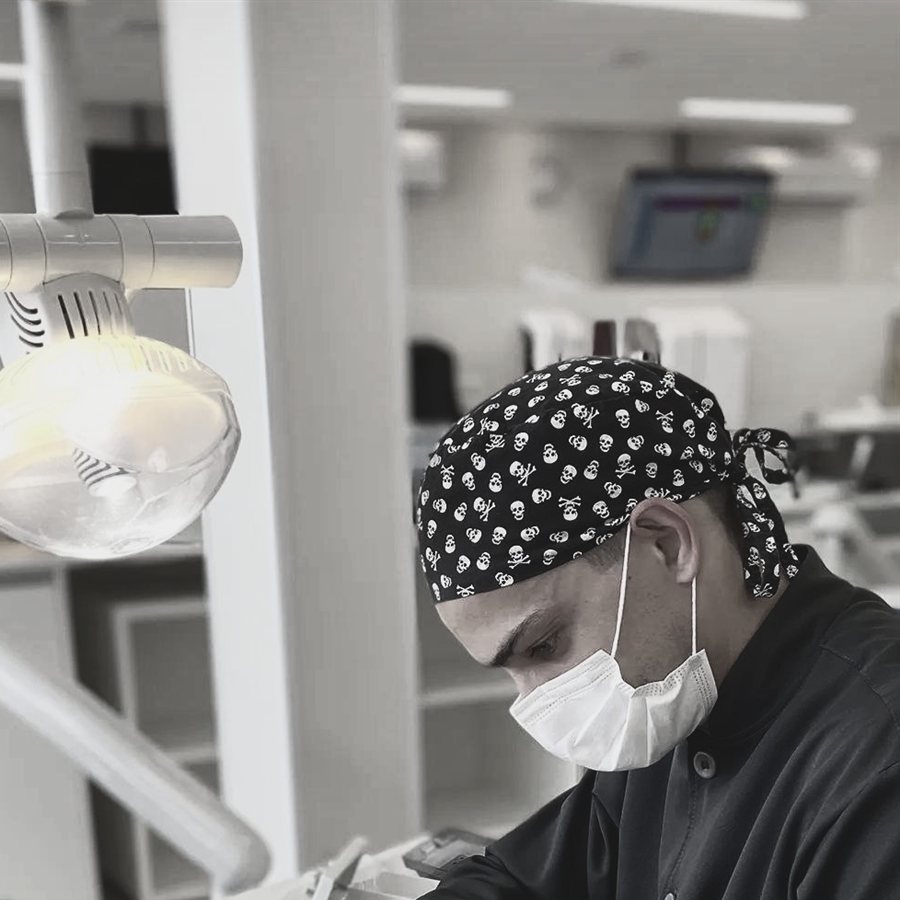 Dr. Diogo Bordin, de touca e máscara, concentrado durante um atendimento sob a luz do refletor